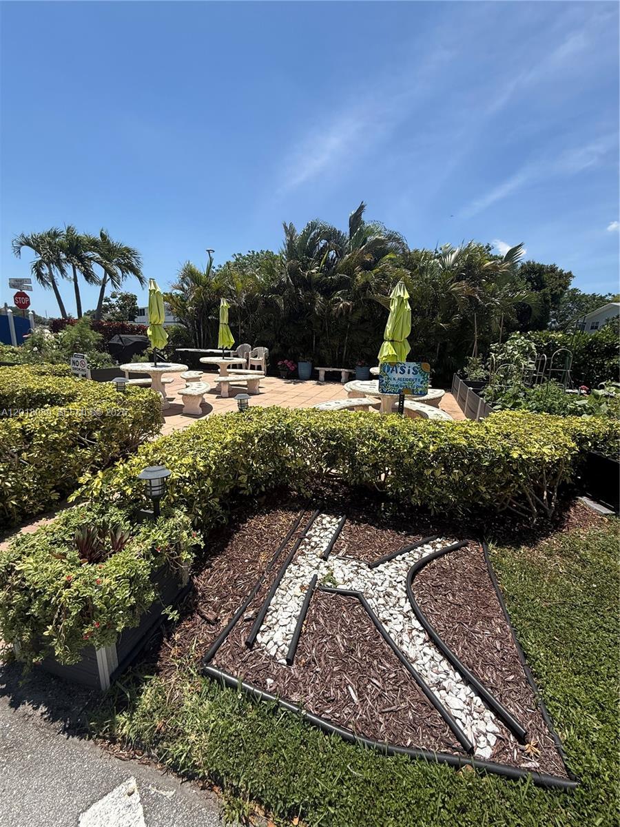 An outdoor patio area features stone tables with umbrellas and a landscaped letter K — 4047 Lyndhurst K # 4047, Deerfield Beach FL 33442, DEERFIELD BEACH, FL