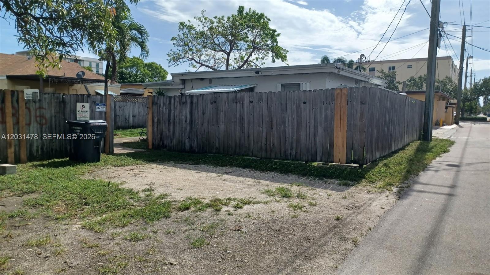 A wooden fence encloses a single-story house next to a gravel driveway and alleyway — 1806 Funston St # B, Hollywood FL 33020, HOLLYWOOD, FL