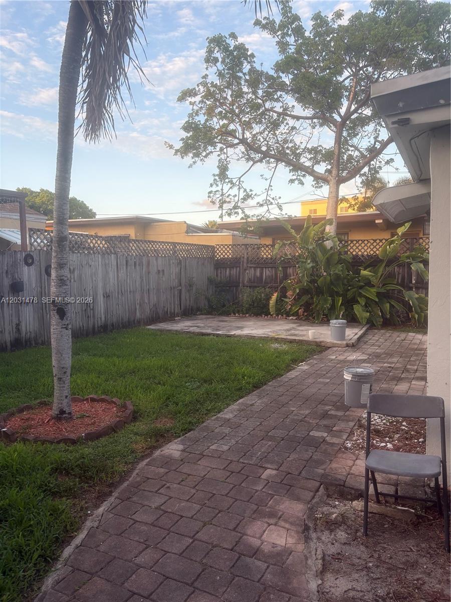 A backyard features a paved walkway, a concrete patio, a palm tree, and wooden fencing — 1806 Funston St # B, Hollywood FL 33020, HOLLYWOOD, FL