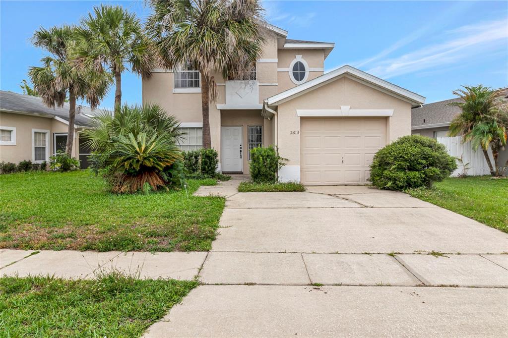 A two-story suburban house features a beige stucco exterior, a single-car garage, and palm trees — 2613 SPRING HILL DRIVE, KISSIMMEE, FL