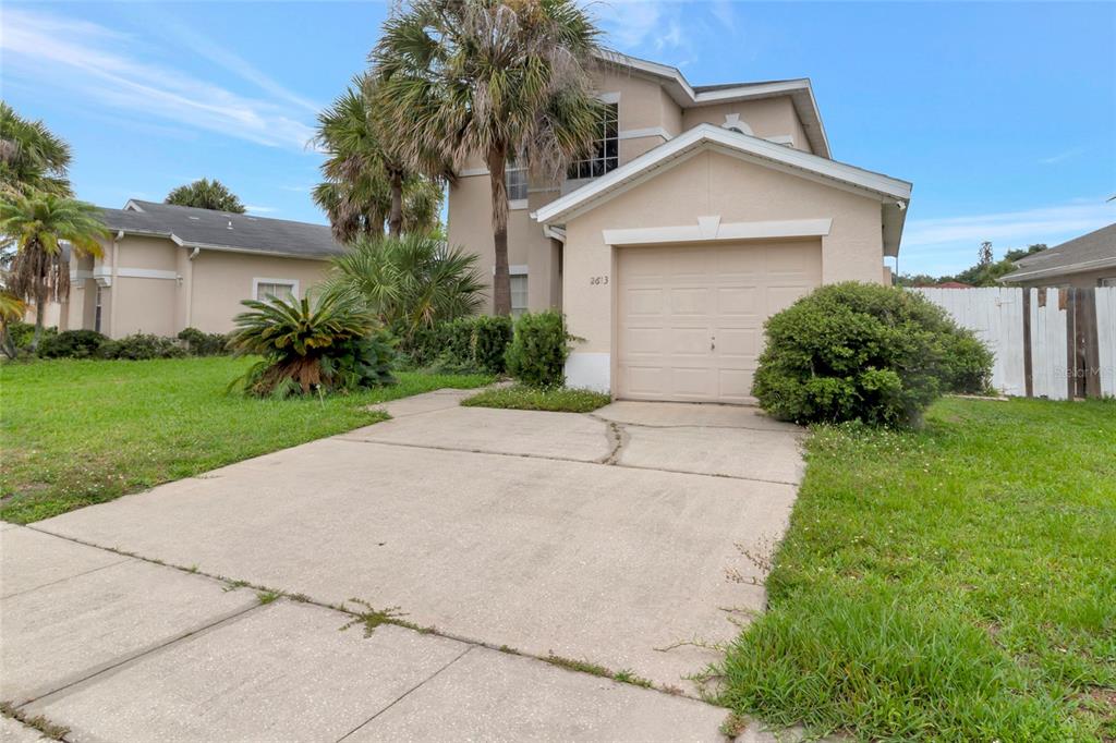 A two-story house with a beige stucco exterior, a single-car garage, and a concrete driveway — 2613 SPRING HILL DRIVE, KISSIMMEE, FL