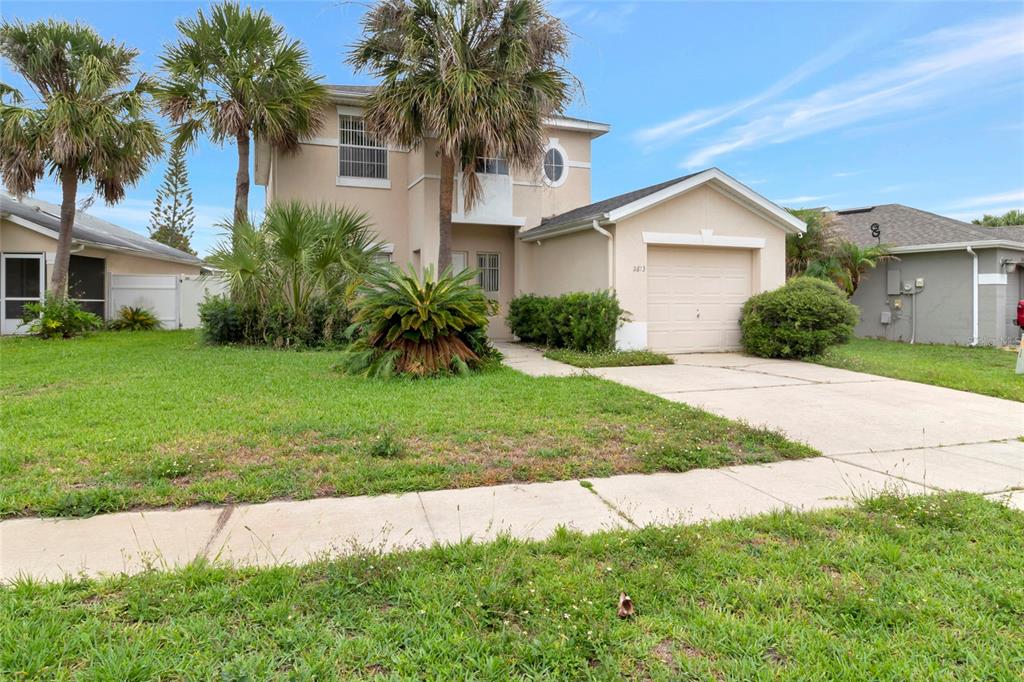 A two-story house with a beige exterior, a one-car garage, and palm trees in front — 2613 SPRING HILL DRIVE, KISSIMMEE, FL