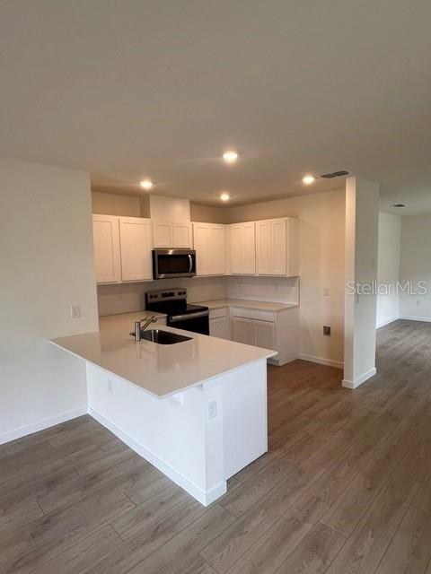 A kitchen features white cabinets, a quartz countertop island, and light wood-look flooring — 1365 CAMELLIA BLOOM LANE, SANFORD, FL