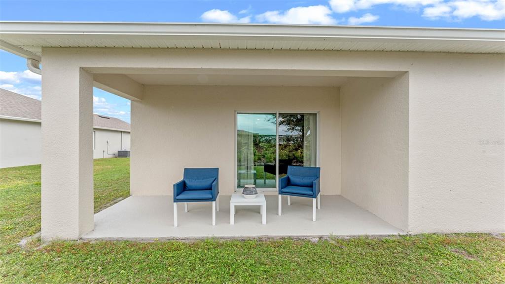 A covered concrete patio features two blue chairs and a small table by a sliding door — 1365 CAMELLIA BLOOM LANE, SANFORD, FL