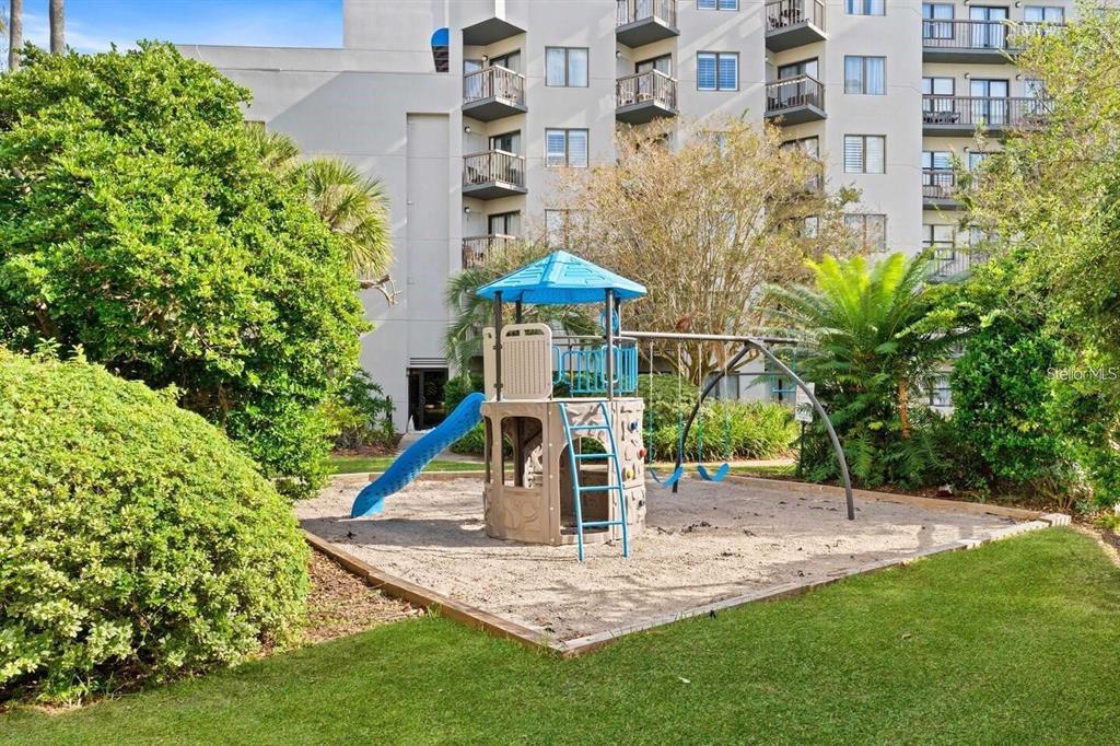 A playground with a blue-roofed climbing structure and slide sits on a sandy lot — 6165 CARRIER DRIVE UNIT 2103, ORLANDO, FL