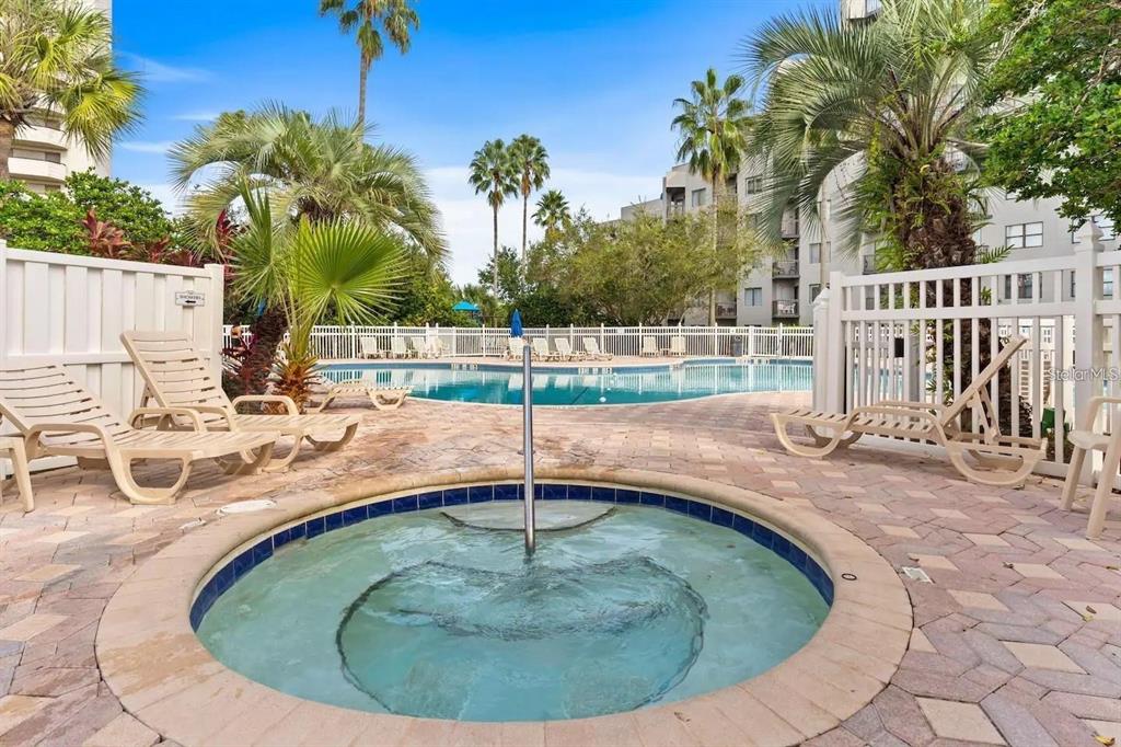 A circular hot tub sits on a brick patio in front of a swimming pool — 6165 CARRIER DRIVE UNIT 2103, ORLANDO, FL