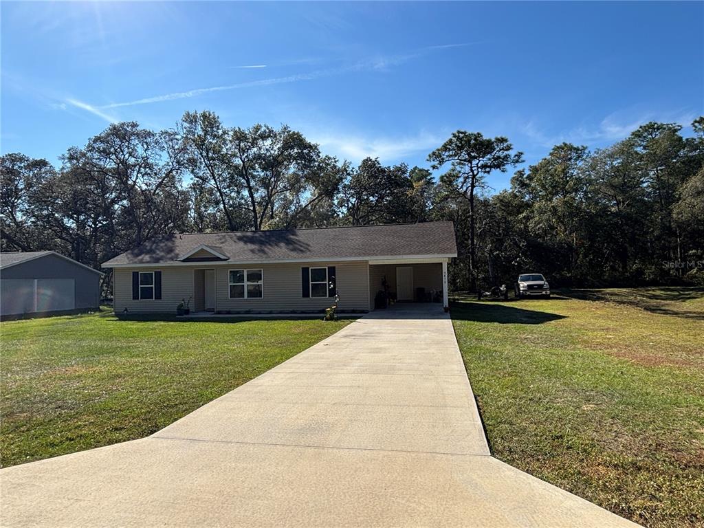 A single-story house with beige siding, a concrete driveway, and a carport sits on a lawn — 5870 SE 171ST COURT, OCKLAWAHA, FL