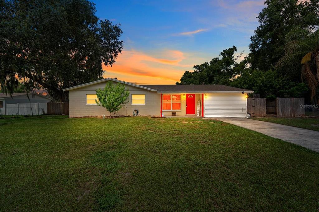A single-story house with a white garage, red front door, and a large front lawn — 4710 JOYCE DRIVE, LAKELAND, FL