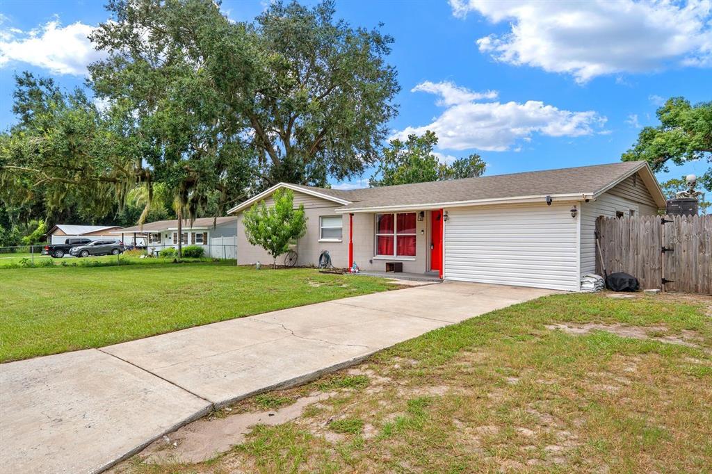 A single-story house with a concrete driveway, a red front door, and a wooden fence — 4710 JOYCE DRIVE, LAKELAND, FL
