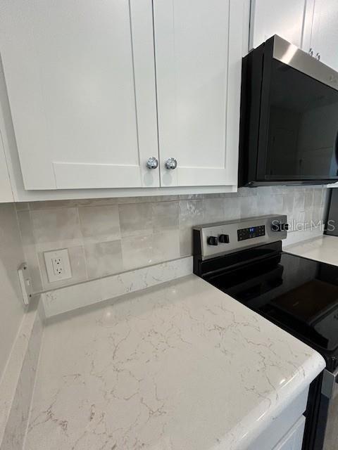 A kitchen features white cabinets, a light-colored quartz countertop, and a stainless steel stove — 6163 DAVID BOULEVARD, PORT CHARLOTTE, FL