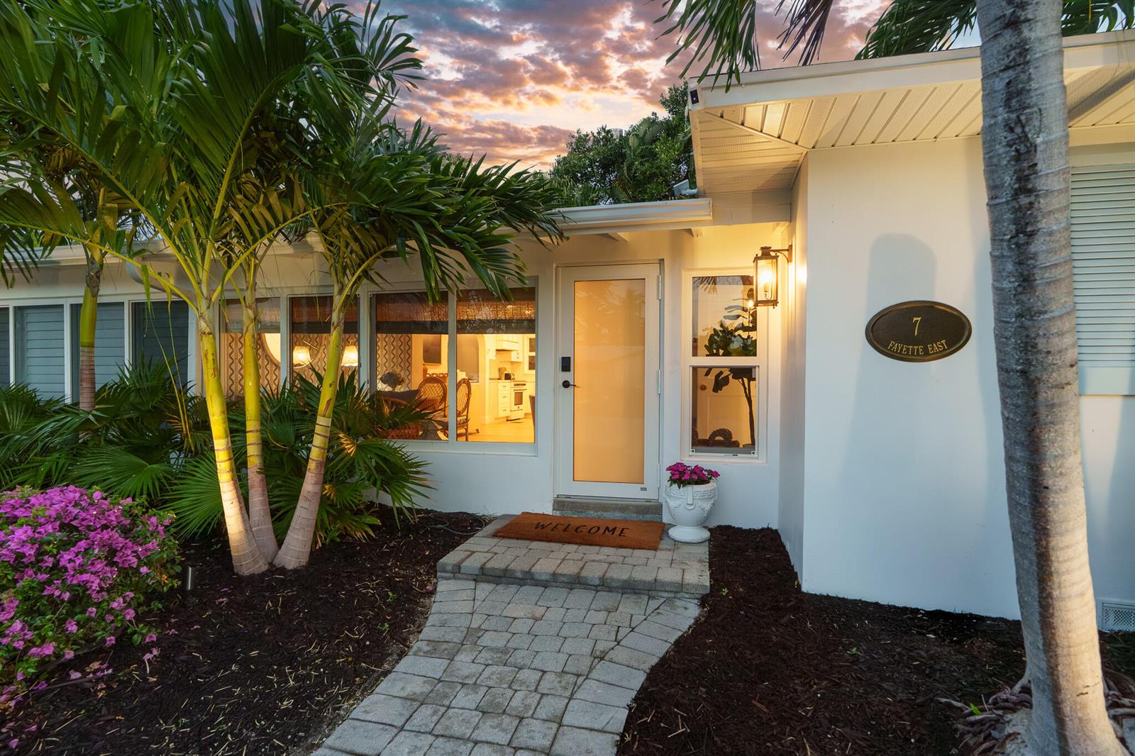 A paved walkway leads to the front entrance of a white house with palm trees — 7 Fayette Drive, Boynton Beach FL 33435, BOYNTON BEACH, FL