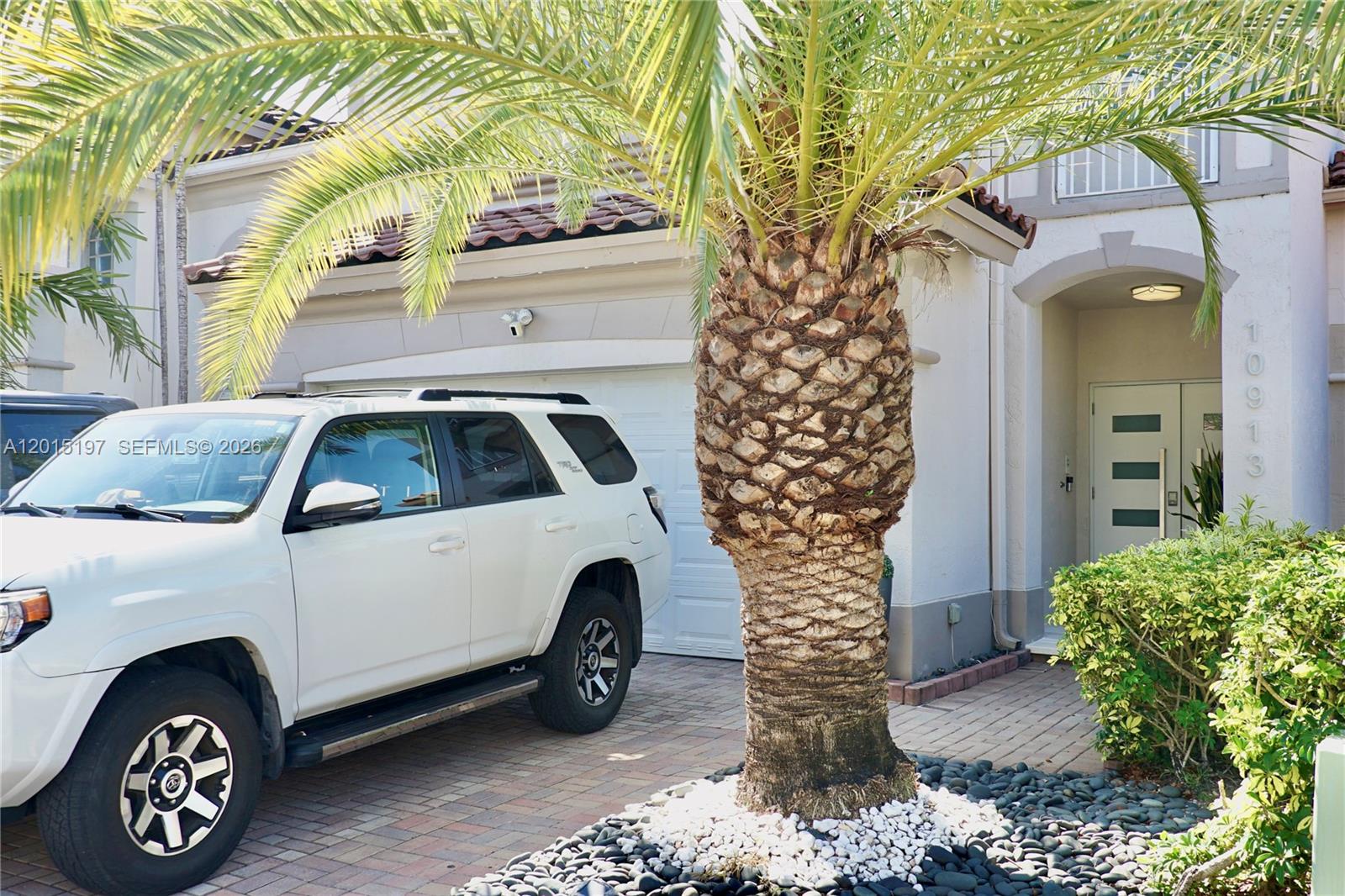A white SUV is parked in the driveway in front of a house with a palm tree — 10913 NW 67th St, Doral FL 33178, DORAL, FL