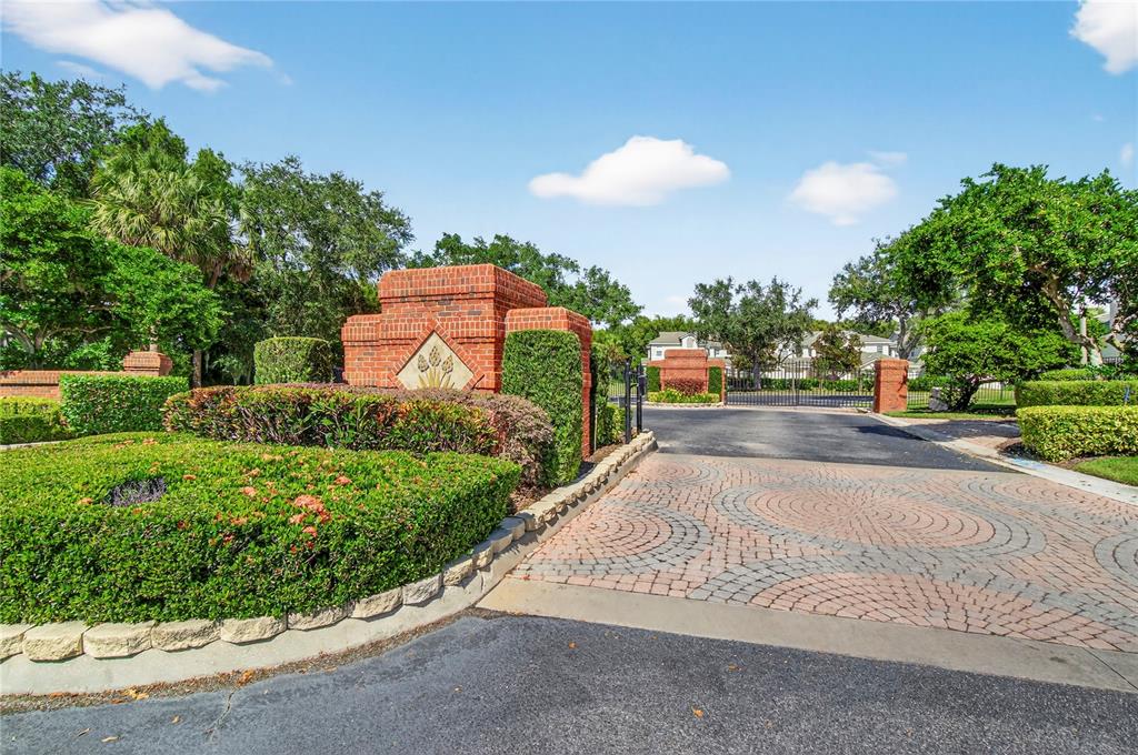 A brick entrance monument stands at the gated driveway of a residential community — 516 GRASSLANDS VILLAGE CIRCLE, LAKELAND, FL