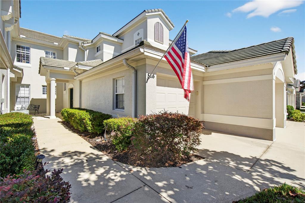 A beige two-story townhouse exterior features a garage, a sidewalk, and an American flag — 516 GRASSLANDS VILLAGE CIRCLE, LAKELAND, FL