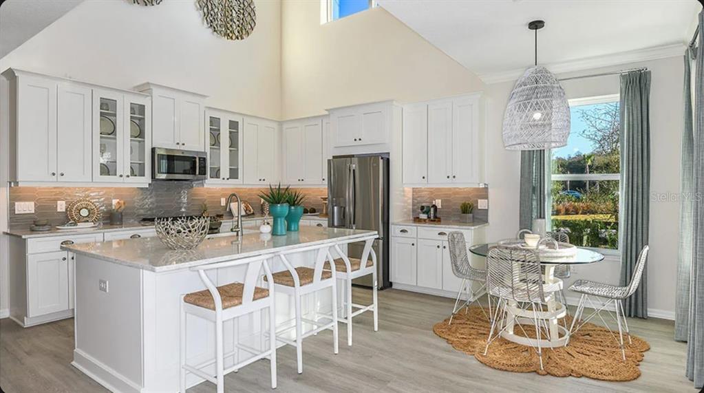 A bright kitchen features white cabinetry, a large island with bar seating, and a dining area — 5156 DOMINION ALLEY, ST CLOUD, FL