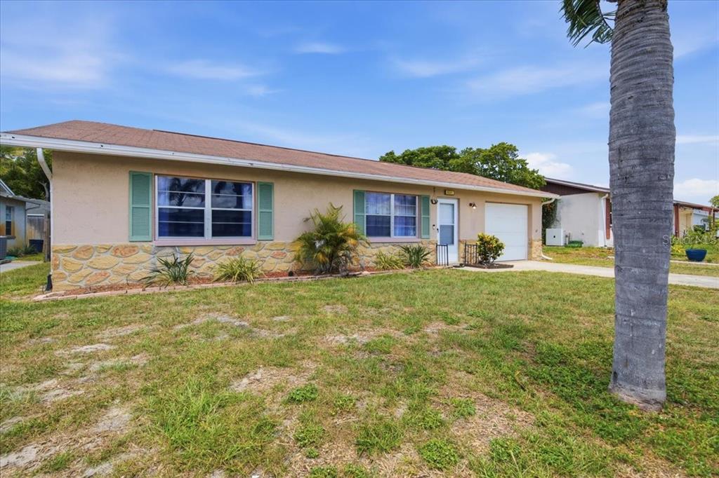 A single-story house with a tan stucco exterior, stone accents, and a small attached garage — 5051 BROOKSIDE LANE, NEW PORT RICHEY, FL