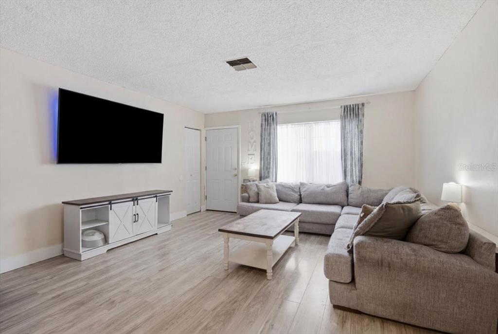A living room features light wood flooring, a gray sectional sofa, and a wall-mounted television — 5051 BROOKSIDE LANE, NEW PORT RICHEY, FL
