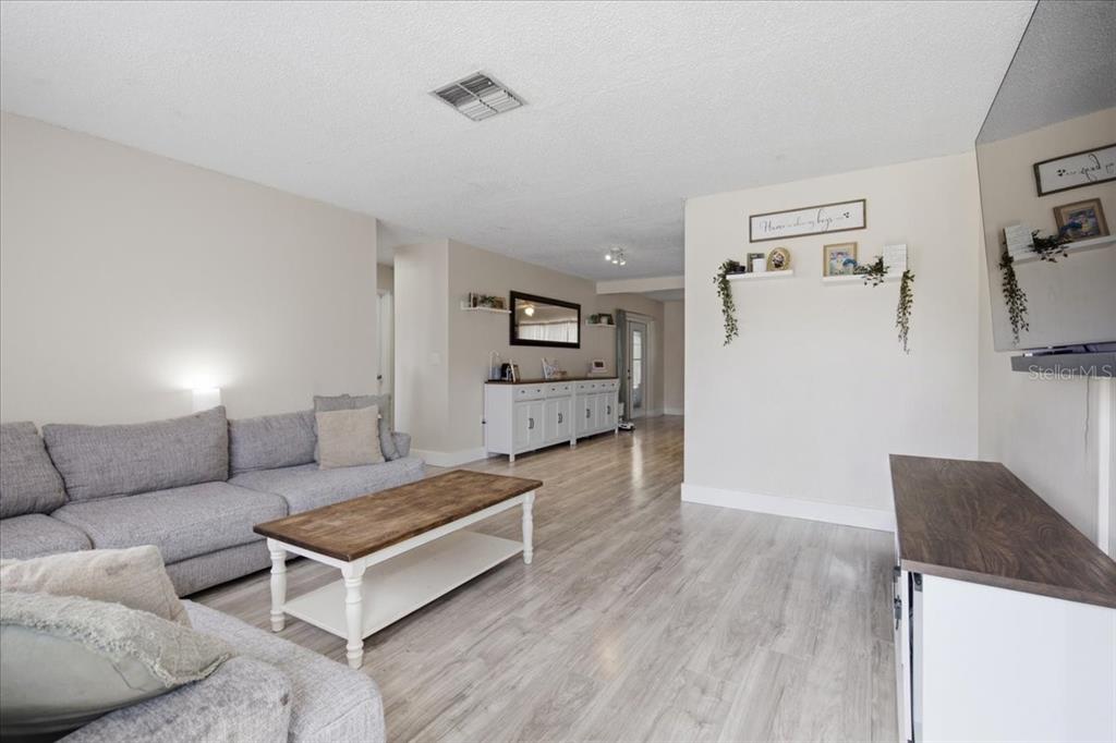 A living room features light wood-look flooring, a gray sectional sofa, and a coffee table — 5051 BROOKSIDE LANE, NEW PORT RICHEY, FL