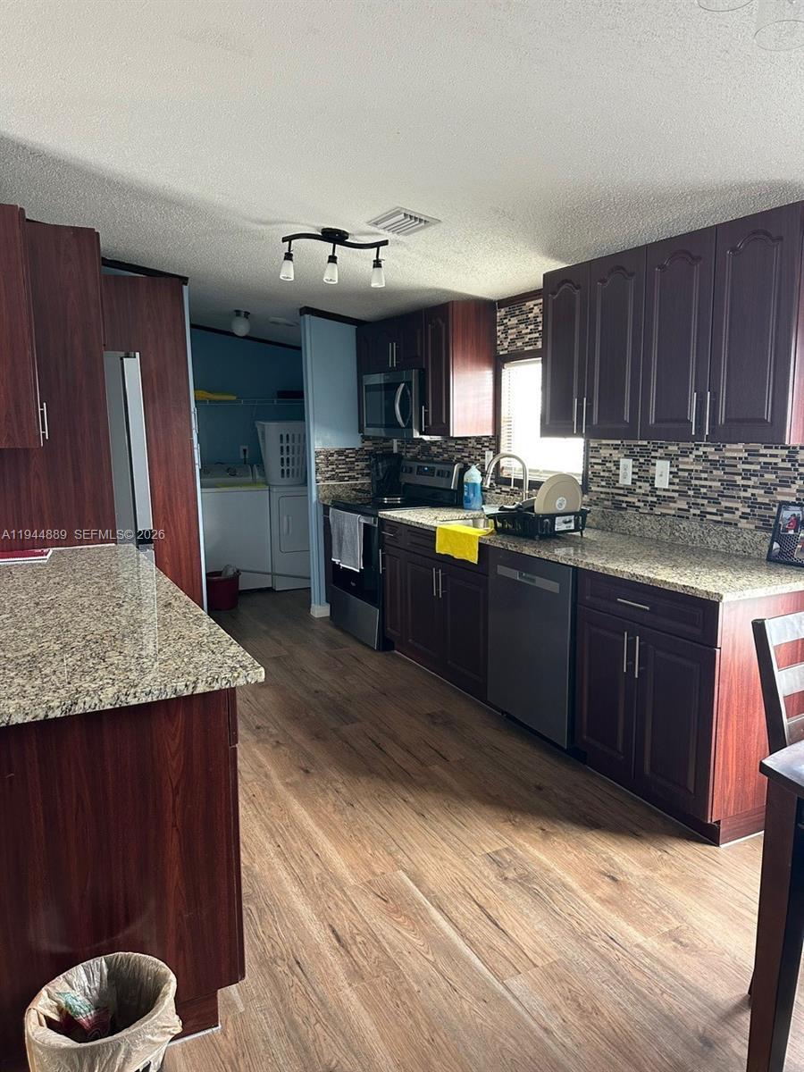 A kitchen features dark wood cabinets, granite countertops, a mosaic backsplash, and stainless steel appliances — 1122 JOHNSON RD, Clewiston FL 33440, CLEWISTON, FL