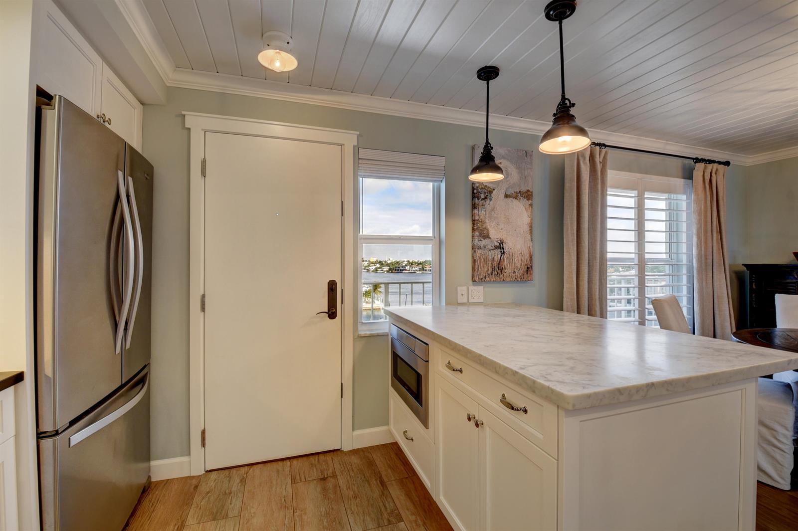 A kitchen features a marble-topped island, stainless steel refrigerator, and a view of the water — 1 Harbourside Drive # 3702, Delray Beach FL 33483, DELRAY BEACH, FL