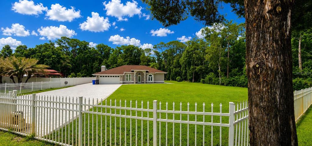 A single-story house with a brown roof sits behind a white fence and green lawn — 2511 PRISCILLA COURT, LUTZ, FL