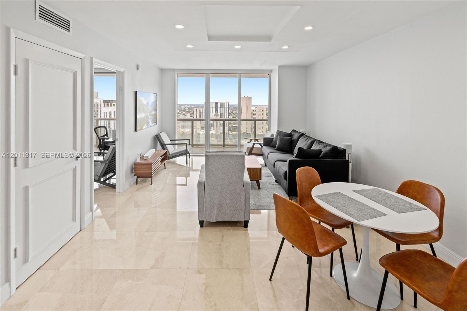 A modern living and dining area features tile floors, a black sofa, and city views — 50 Biscayne Blvd # 4405, Miami FL 33132, MIAMI, FL