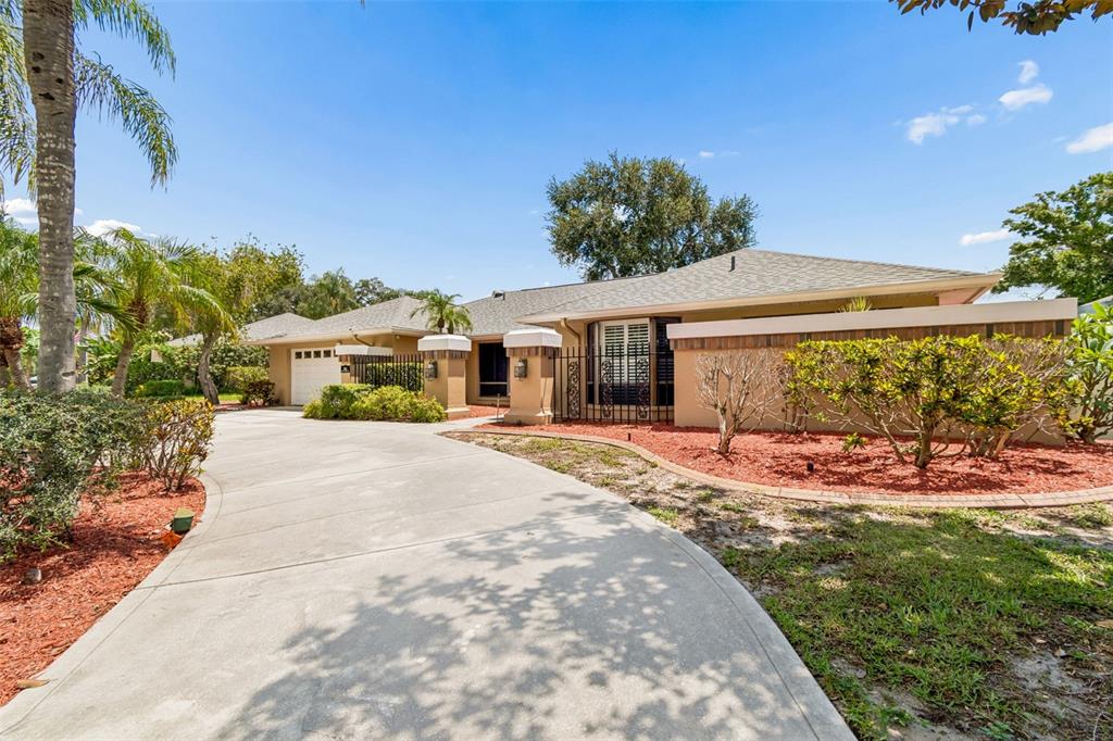 A tan single-story house with a concrete driveway, palm trees, and a fenced front courtyard — 1563 MISTY PLATEAU TRAIL, CLEARWATER, FL