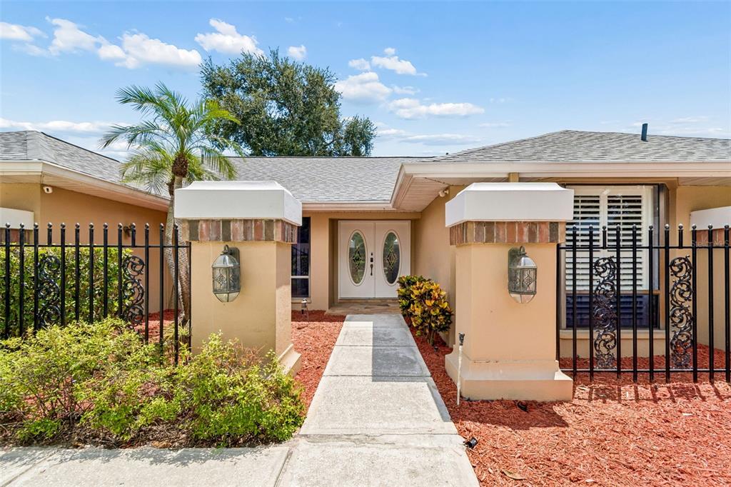 A concrete walkway leads to the double front doors of a tan stucco house — 1563 MISTY PLATEAU TRAIL, CLEARWATER, FL