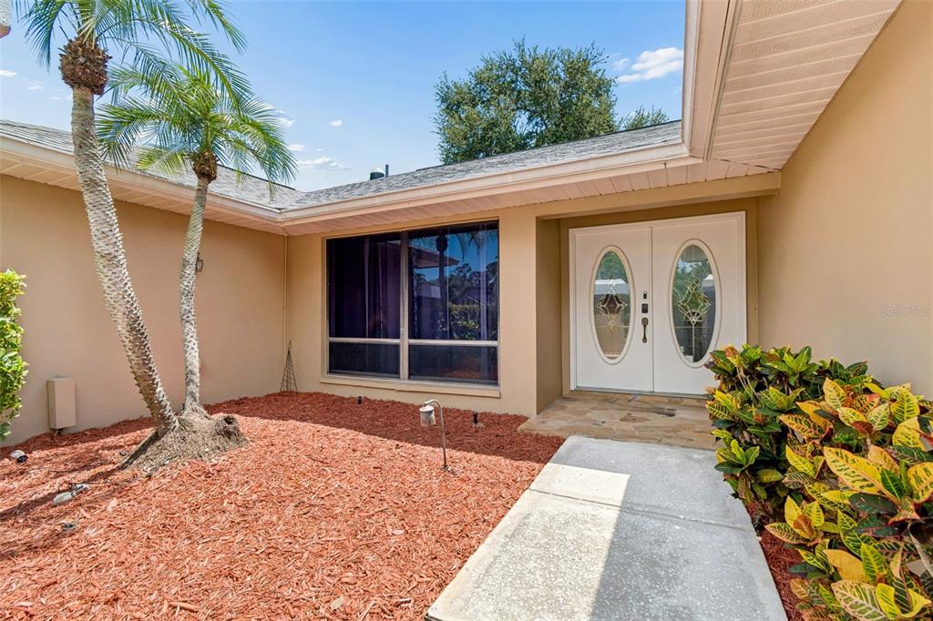 The exterior of a house features a double front door, a large window, and landscaping — 1563 MISTY PLATEAU TRAIL, CLEARWATER, FL