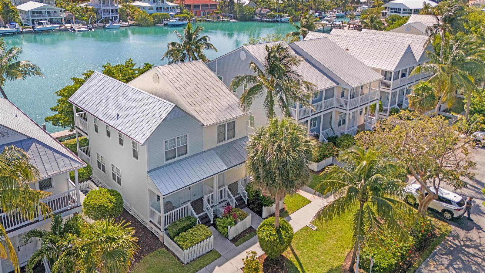 An aerial view shows several light-colored houses with metal roofs situated along a turquoise canal — 7051 Harbor Village Drive, FL 33050, FL