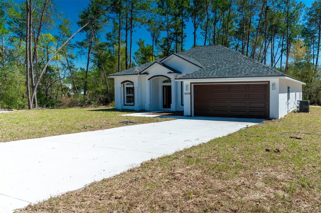 A single-story white house with a brown garage door sits on a grassy lot — 16559 SW 48TH TERRACE, OCALA, FL