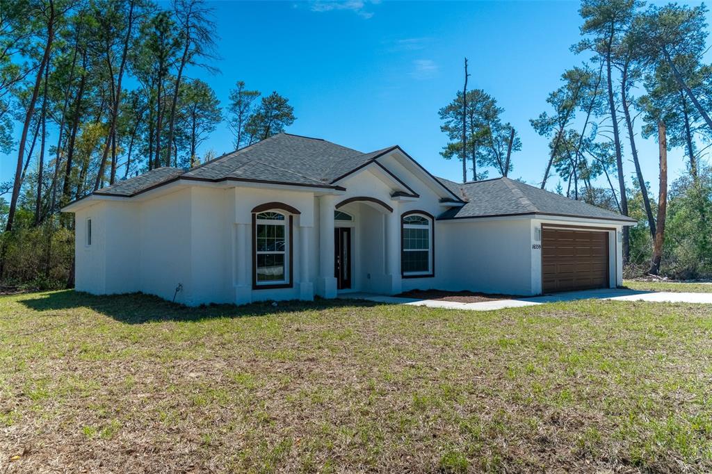 A single-story white stucco house with a brown garage door and dark roof shingles — 16559 SW 48TH TERRACE, OCALA, FL