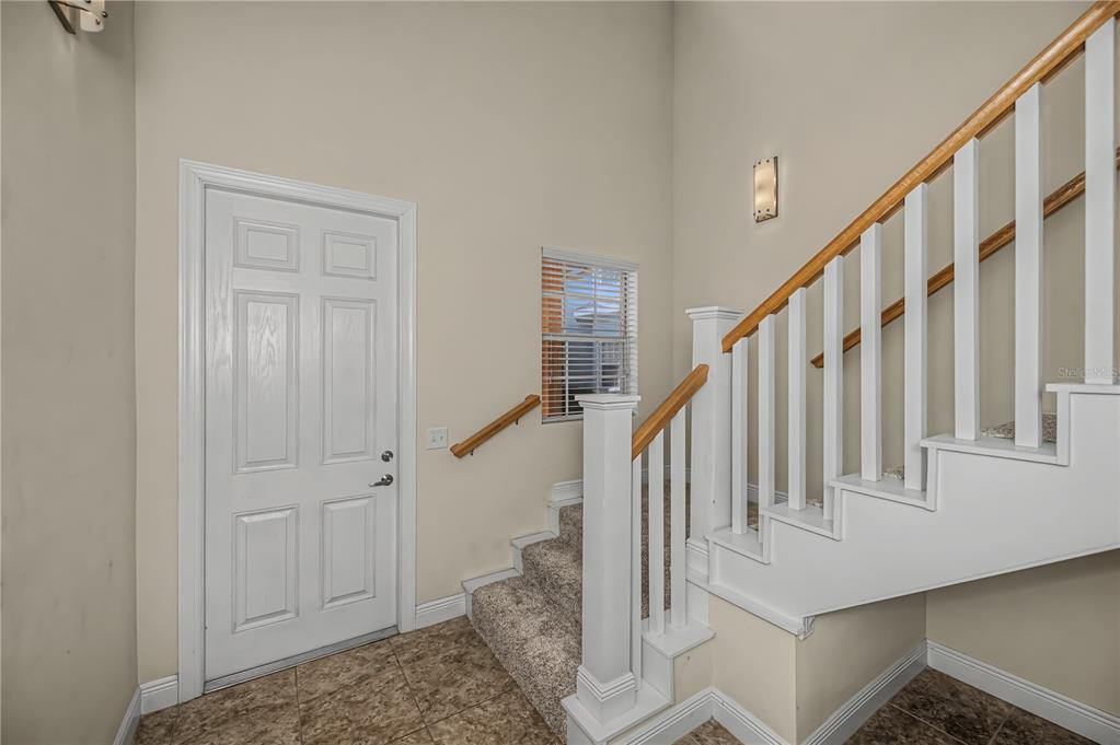 An entryway features a white door, tiled floor, carpeted stairs, and a wooden handrail — 25601 HERITAGE LAKE BOULEVARD UNIT 46, PUNTA GORDA, FL