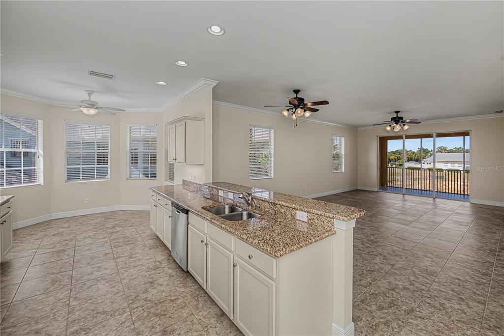 A kitchen with granite countertops and tile flooring opens to a living area with ceiling fans — 25601 HERITAGE LAKE BOULEVARD UNIT 46, PUNTA GORDA, FL