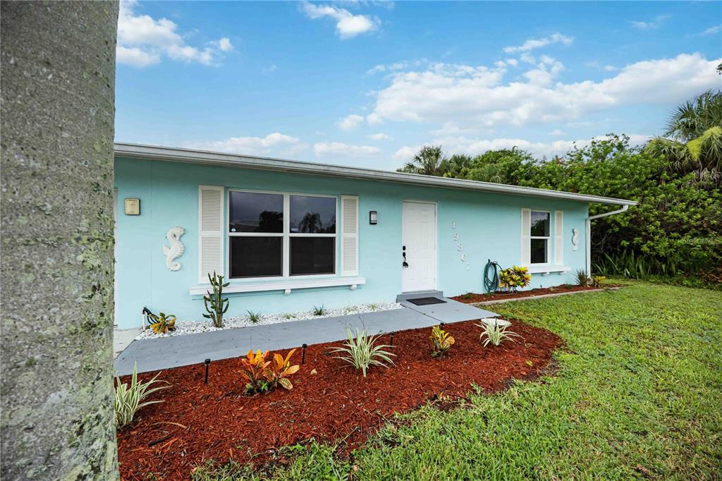 A light blue single-story house features a white front door, shutters, and landscaped mulch beds — 19367 EDGEWATER DRIVE, PORT CHARLOTTE, FL