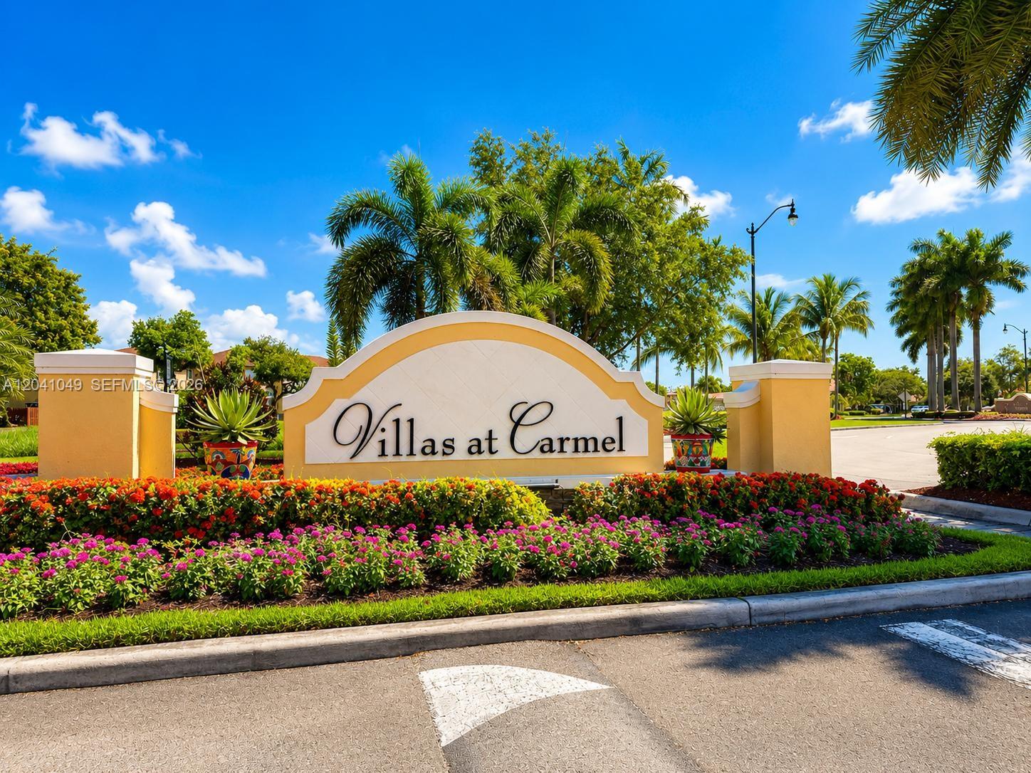 A sign for Villas at Carmel stands behind a garden bed with colorful flowers — HOMESTEAD, FL