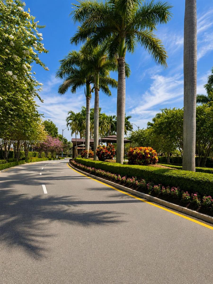 A paved road leads toward a gated entrance lined with palm trees and manicured landscaping — HOMESTEAD, FL