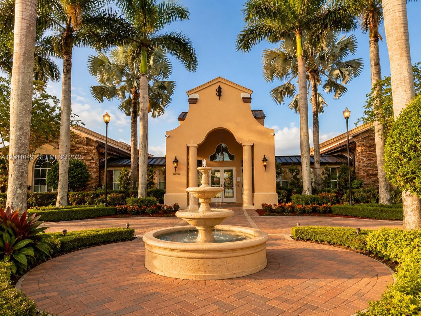 A tiered stone fountain sits in front of a tan building entrance with palm trees — HOMESTEAD, FL