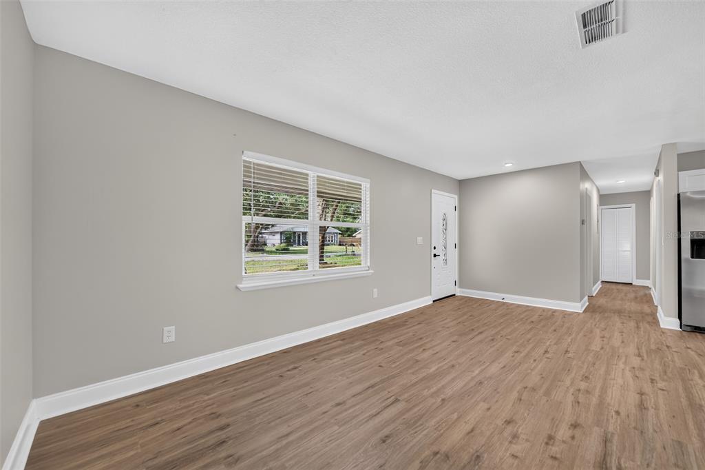 A living room with light gray walls, wood-look flooring, a window, and an entry door — 262 MARJORIE BOULEVARD, LONGWOOD, FL