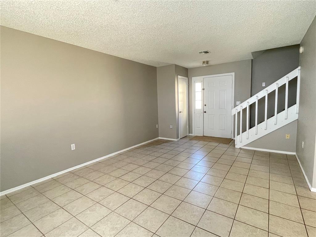 An empty room with beige walls, tiled floors, a front door, and a white staircase — 687 LAKE DEXTER CIRCLE, WINTER HAVEN, FL