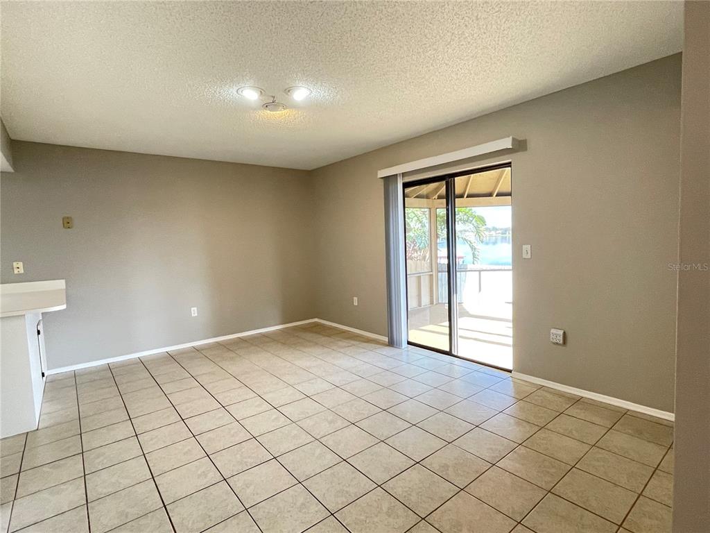 An empty room with beige tile flooring, neutral walls, and a sliding glass door to a patio — 687 LAKE DEXTER CIRCLE, WINTER HAVEN, FL