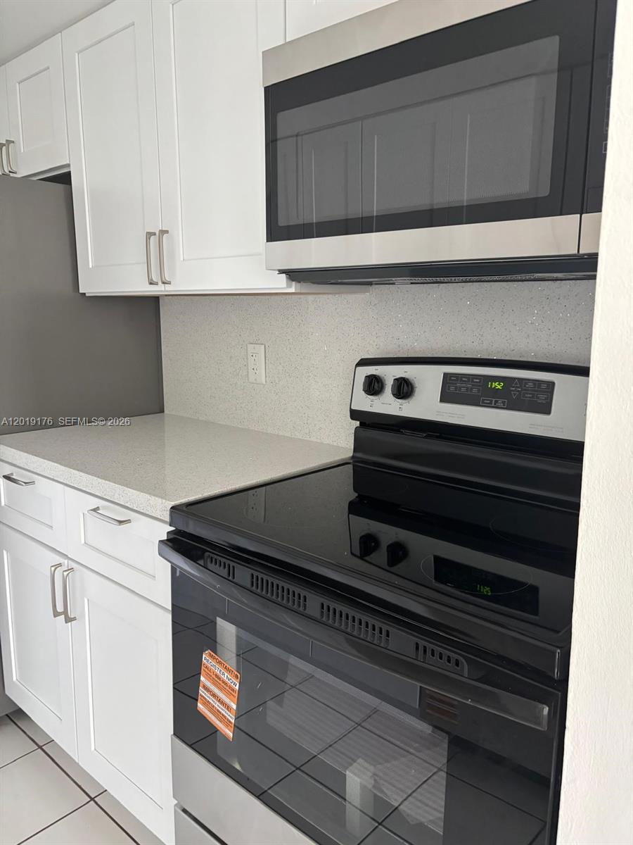 A kitchen features white cabinets, a stainless steel microwave, and a black electric stove — NORTH MIAMI, FL