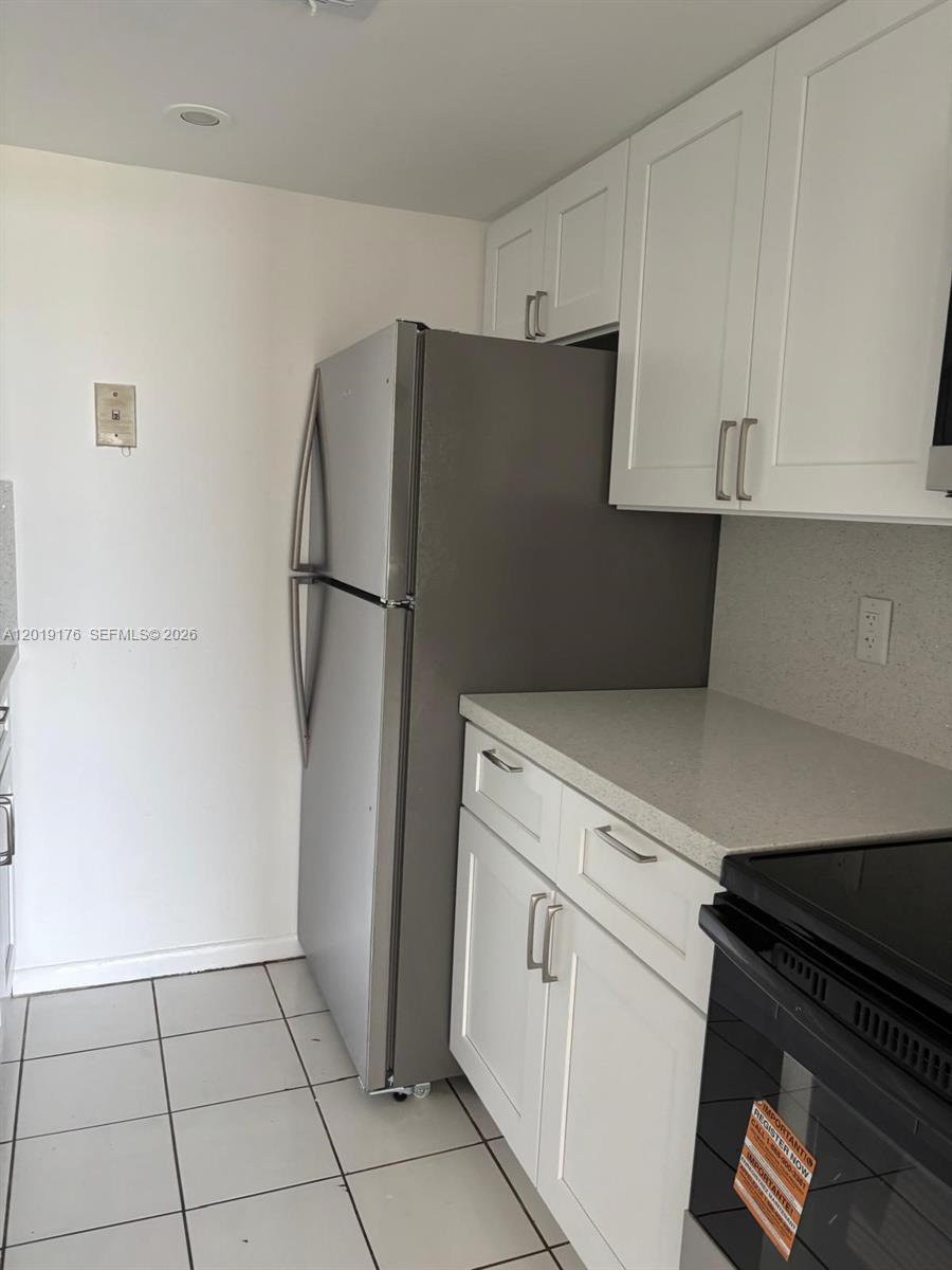 A kitchen features white cabinets, a stainless steel refrigerator, and light-colored countertops — NORTH MIAMI, FL