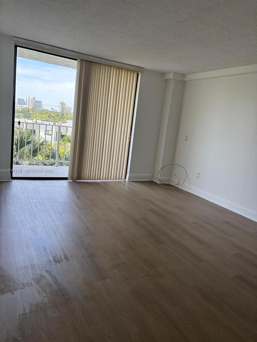 An empty room features light wood-look flooring, white walls, and a sliding glass balcony door — NORTH MIAMI, FL