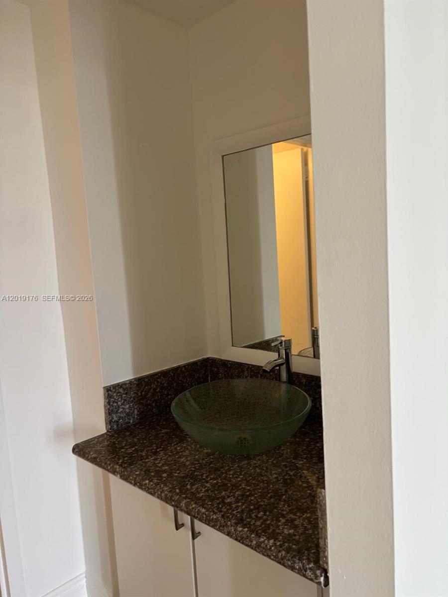 A bathroom vanity features a glass vessel sink, a granite countertop, and a wall mirror — NORTH MIAMI, FL