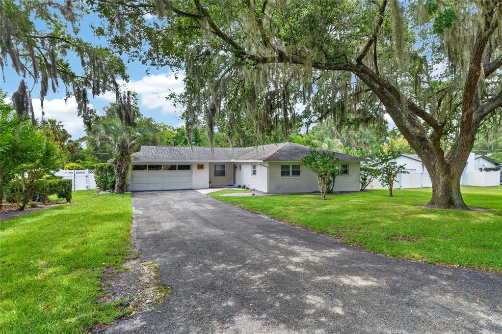 A single-story white brick house with a paved driveway and large moss-draped oak trees — 1502 SE 16TH AVENUE, OCALA, FL