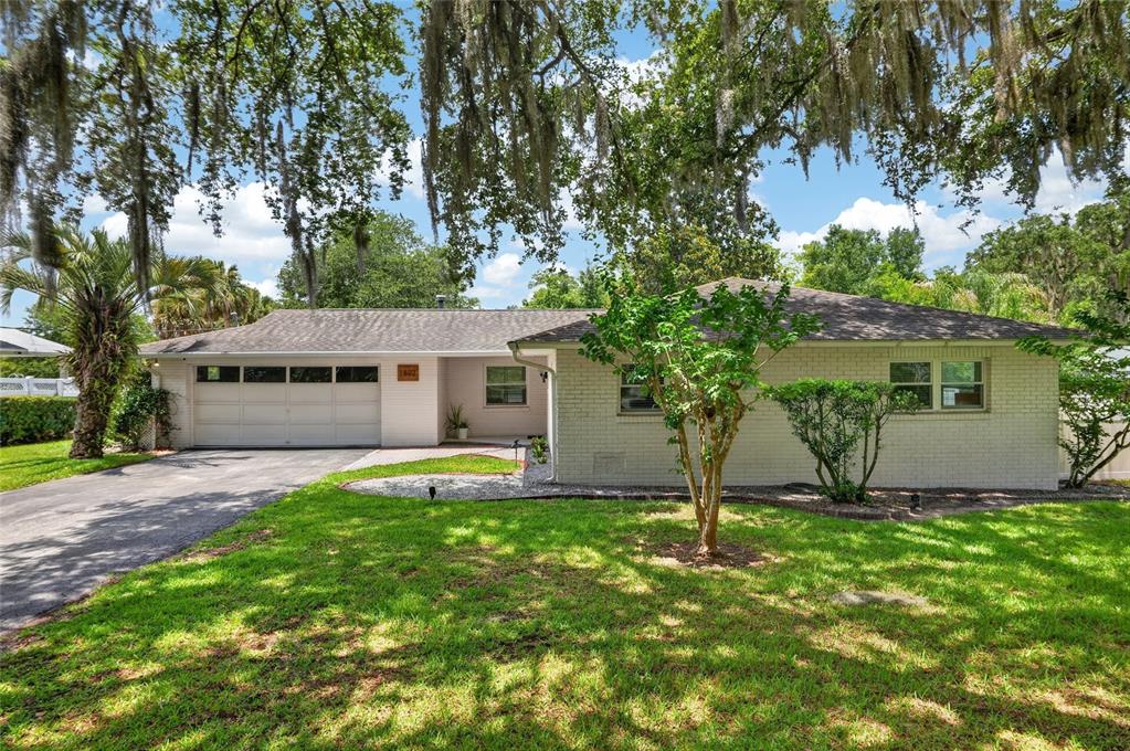 A single-story white brick house with a garage and a large lawn under oak trees — 1502 SE 16TH AVENUE, OCALA, FL
