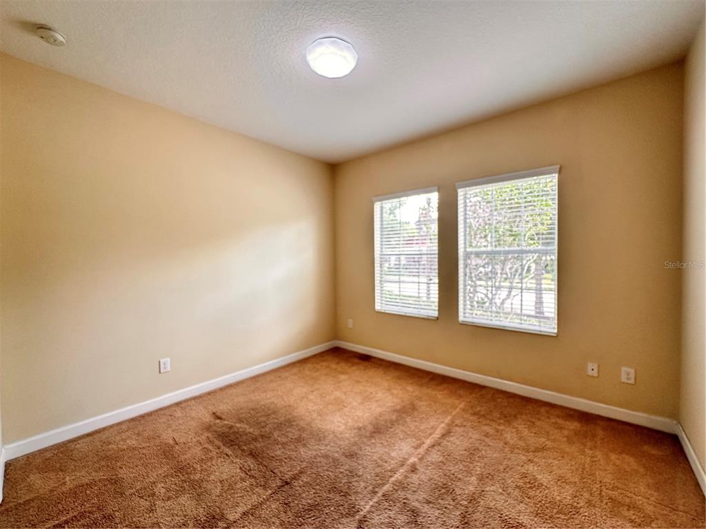 An empty bedroom features tan walls, brown carpeting, and two windows with white blinds — 7409 FAIRGROVE AVENUE, WINDERMERE, FL