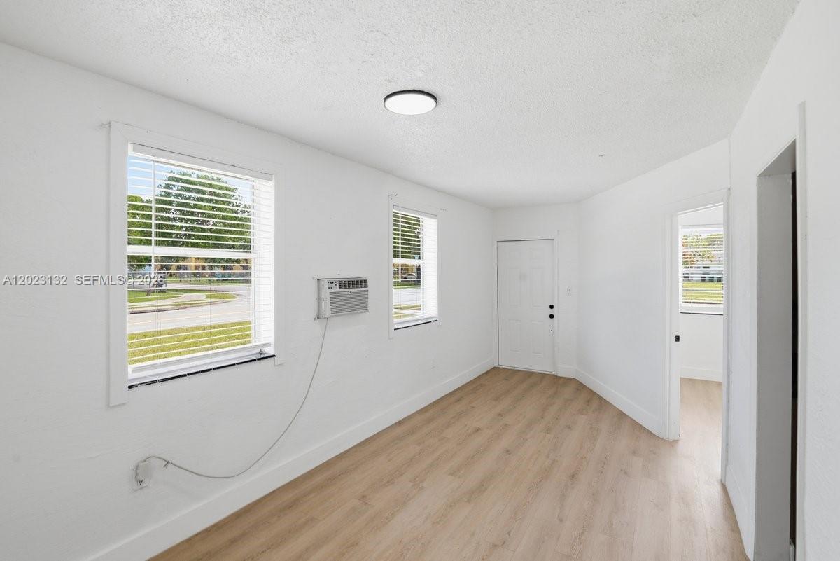 A bright, empty room features white walls, light wood-look flooring, and a window air conditioner — 17875 SW 103rd Ave, Miami FL 33157, MIAMI, FL