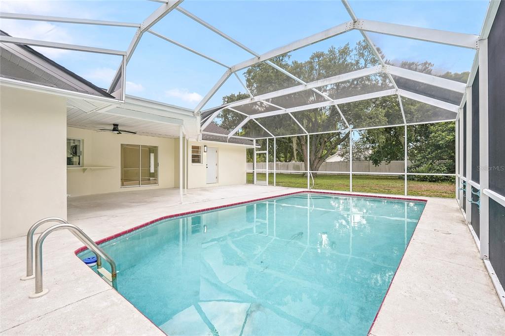 A swimming pool with a screen enclosure and a covered patio area behind a house — 2462 STEPHANIE DRIVE, SPRING HILL, FL